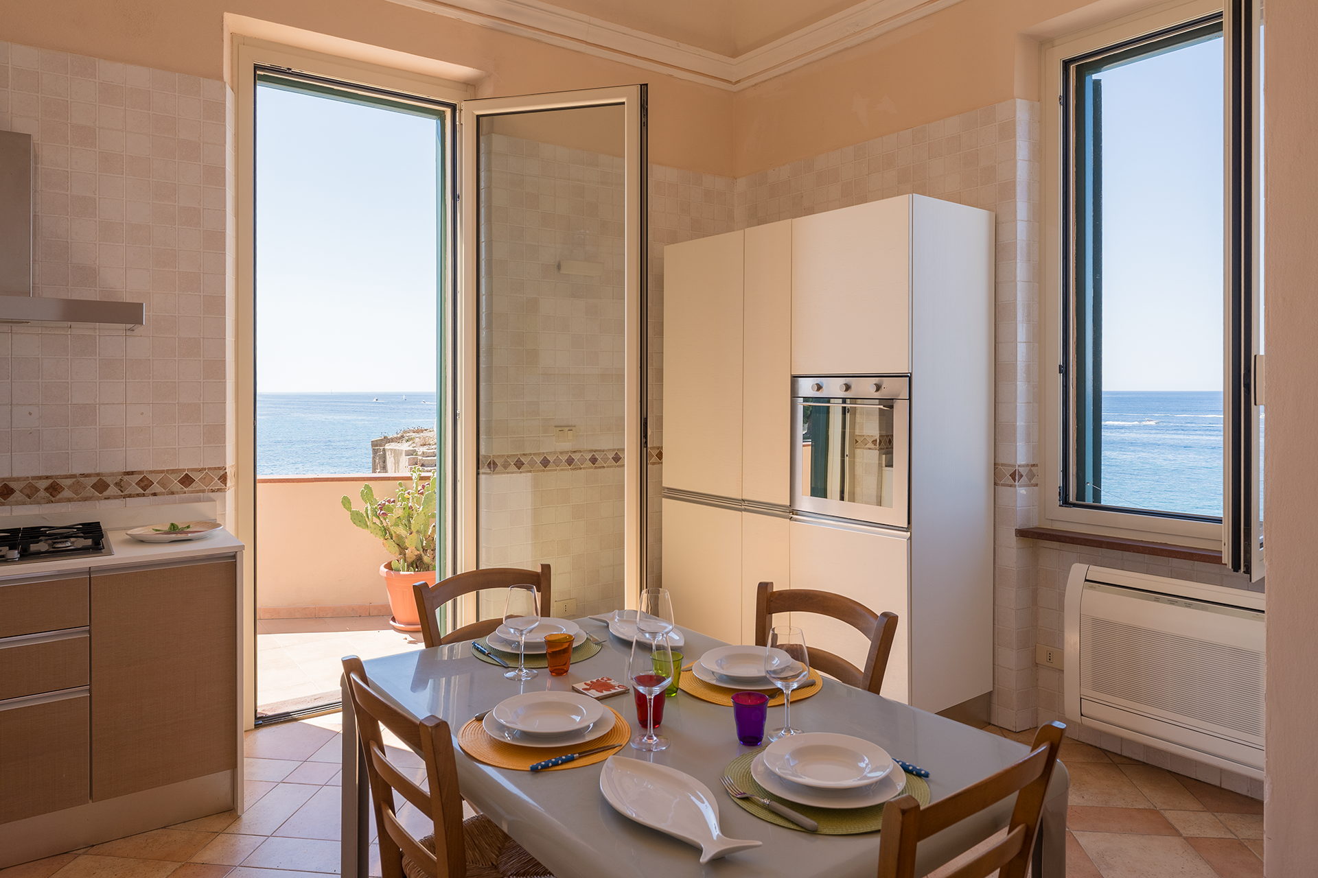Cucina con tavolo apparecchiato, accesso alla terrazza e doppia vista sul mare ad Alghero