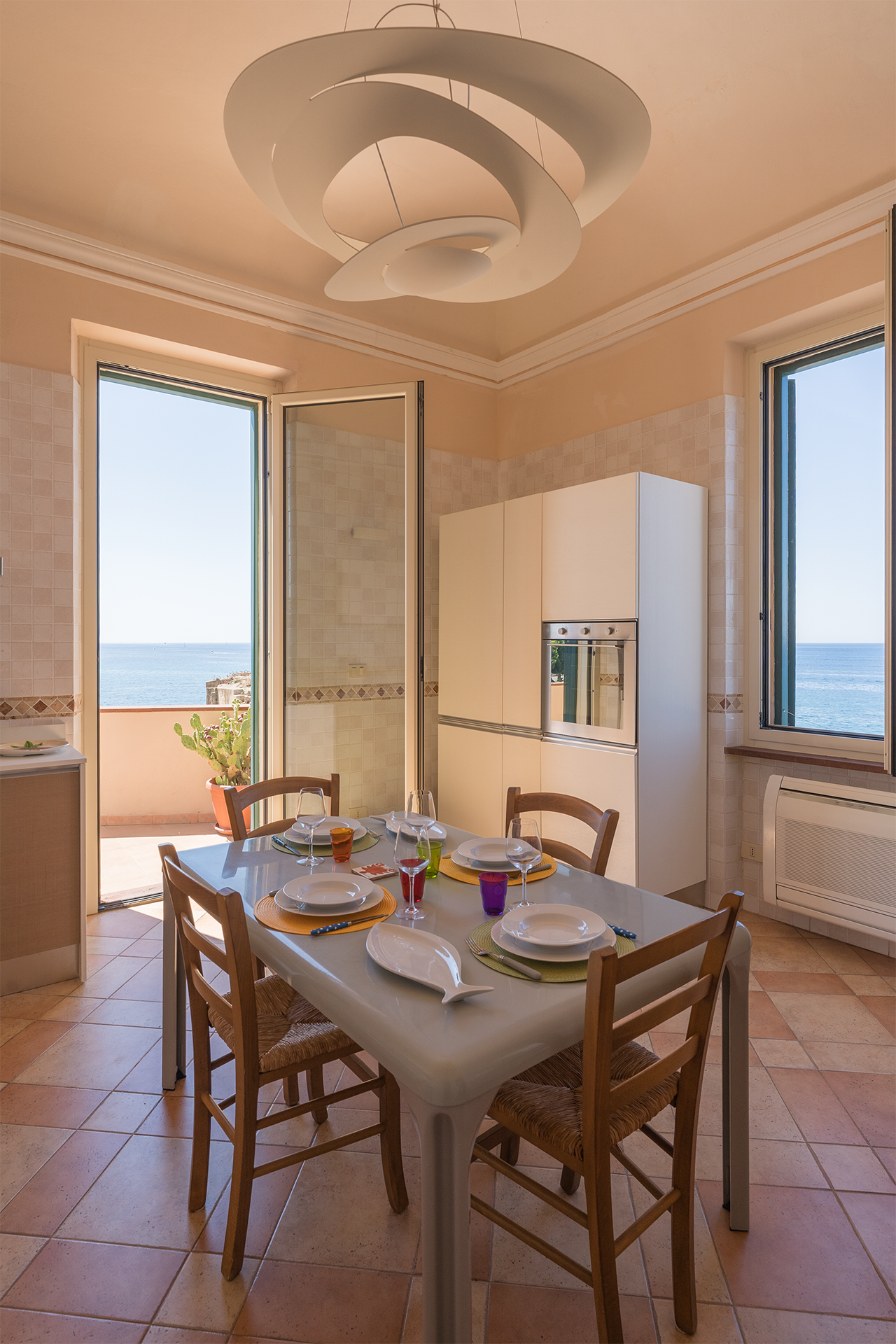 Cucina luminosa con doppio affaccio sul mare Cucina verticale con tavolo apparecchiato, lampada di design e finestre vista mare