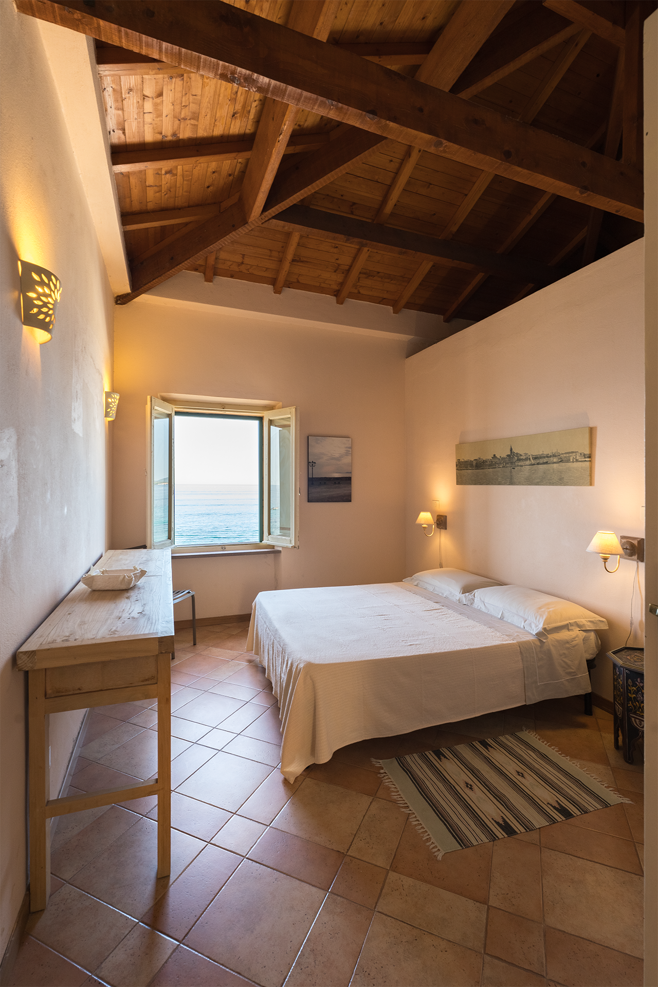 Camera matrimoniale con soffitto in legno e finestra vista mare nell’appartamento L’Attichetto