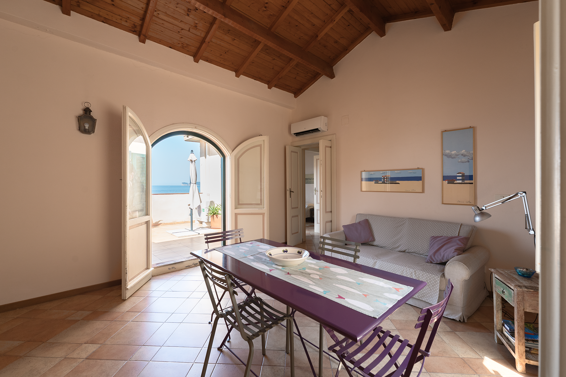 Zona giorno con tavolo, divano e porta ad arco aperta sulla terrazza vista mare